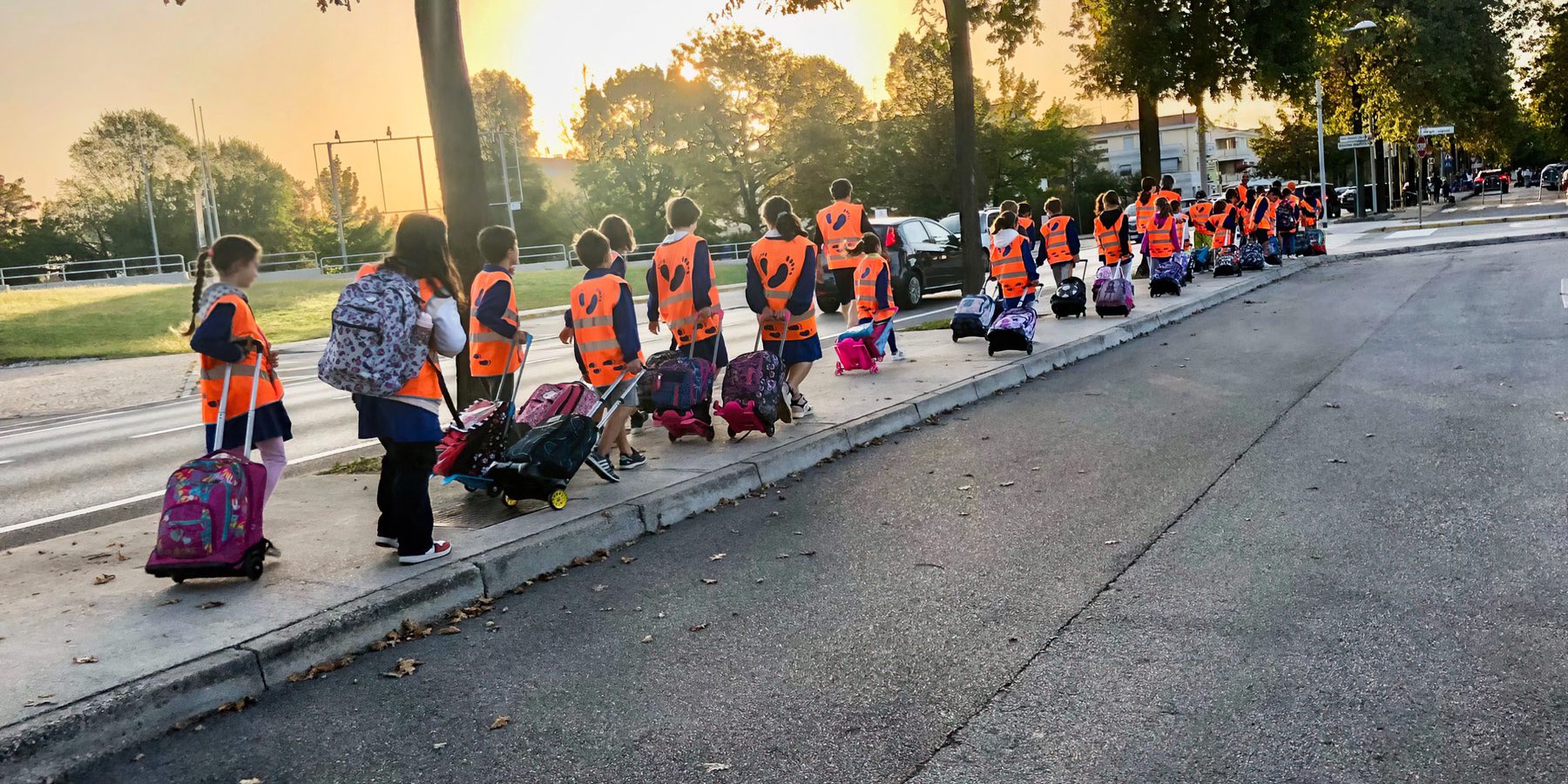 Fila di bambini con pettorina arancione del Pedibus che camminano verso scuola